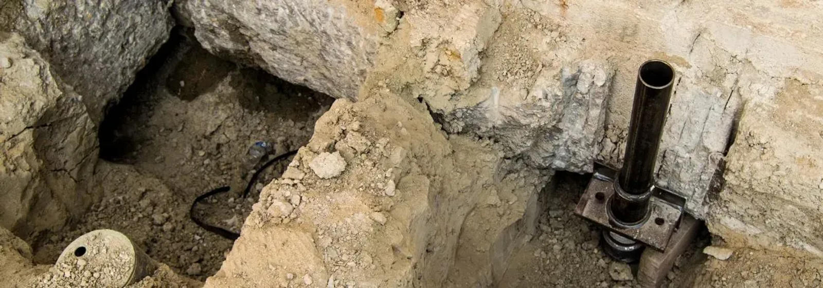 Pipe installation in a rough dirt trench, showcasing a multi-family residential foundation repair case study, with exposed soil and rock.
