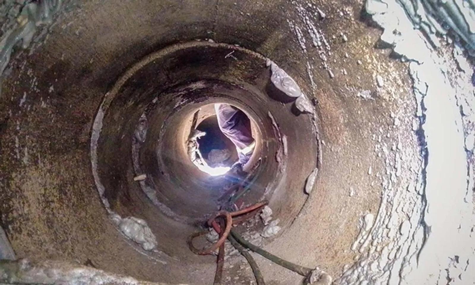 View from inside a pipe showing a person outside, with ropes and a light source illuminating the interior.
