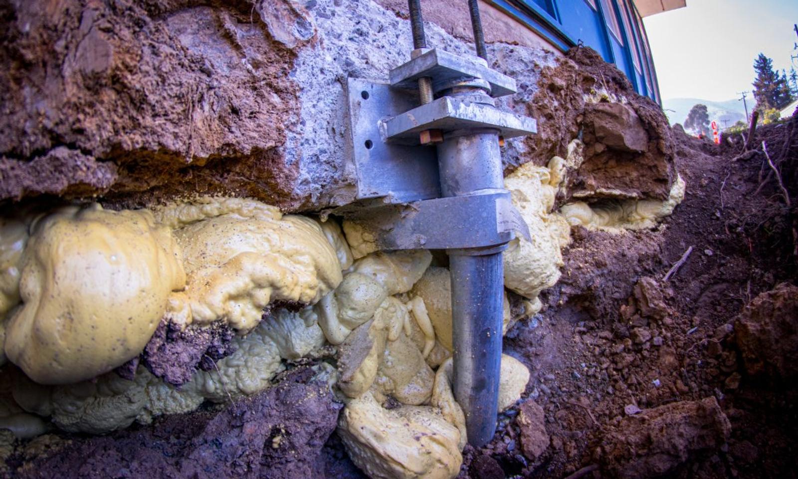 Close-up of a house foundation with metal piling support and expanding foam insulation, showcasing expert commercial foundation repair services.