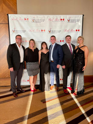 Six people dressed formally pose in front of a banner at an event.