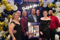 A group of people posing with a poster amid festive balloon decorations and a "Reach for the Stars" sign.