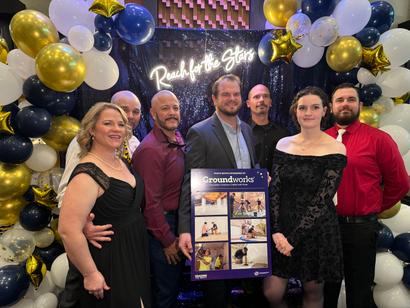 A group of people posing with a poster amid festive balloon decorations and a "Reach for the Stars" sign.