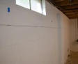 Basement wall with visible horizontal crack and exposed ceiling joists. Small window at the top lets light in.