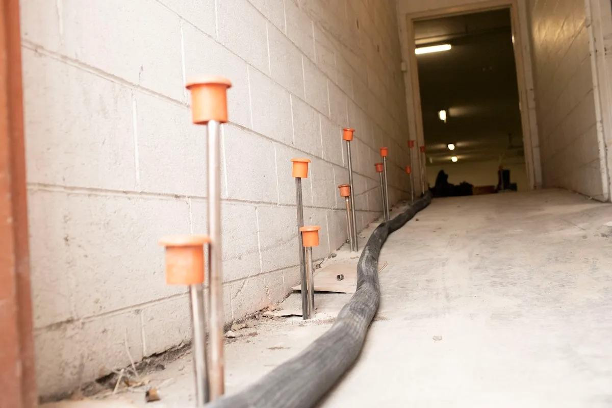 A reinforced concrete wall with metal rods and orange caps ensures ground stabilization, while a black cable runs parallel to the sloping floor.