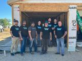 Group of people in front of a partially constructed building, all wearing matching black shirts with green and blue logos.