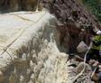 Worker in safety gear sprays insulation foam on rocky hillside; red safety lines are visible.