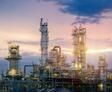 Industrial refinery with tall towers at sunset, surrounded by colorful sky and clouds.