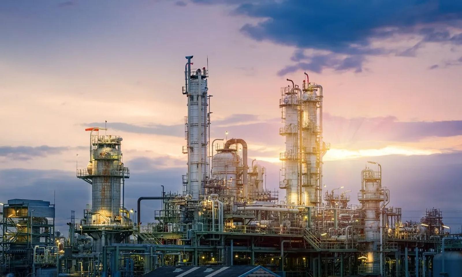Industrial refinery with tall towers at sunset, surrounded by colorful sky and clouds.