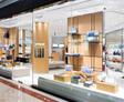 Storefront with large glass windows displaying various handbags and shoes on shelves and pedestals inside a shop.