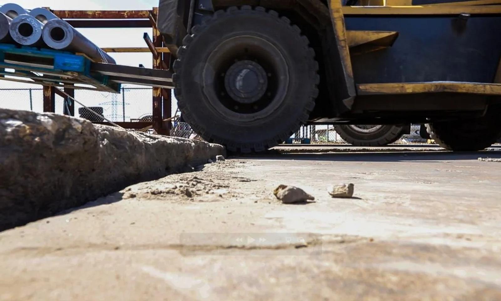 Close-up of a forklift wheel on a construction site, showcasing forklift-friendly slab repair with metal pipes on a nearby rack.