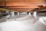 Crawl space with plastic moisture barrier covering the floor and wooden beams overhead.