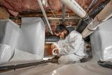 Person in protective suit and headlamp sealing pipes in a crawl space with white tape.