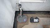 Sump pump system with battery backup installed in a basement with gravel and drainage piping visible.