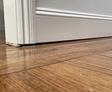 White wall slightly separated over a wooden floor, revealing a small gap.
