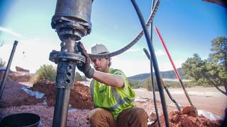 A construction worker in a safety vest operates a large drilling machine, installing Pre-Construction Load-Bearing Helical Piles on a rocky site.