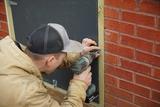Person in a tan jacket using a power drill to secure a crawl space door.
