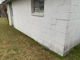 White cinder block building with a window, door, grass lawn, and visible cracks in ceiling alongside the wall.