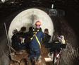 A worker in safety gear sprays material inside a large pipe, bolstering defense infrastructure.