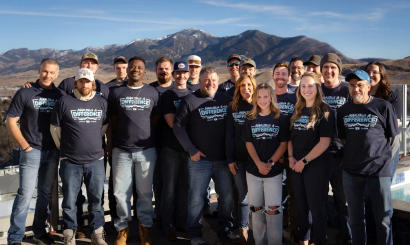 A group of people wearing matching T-shirts poses outdoors with mountains in the background.