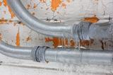 Close-up of icy, frozen metal pipes against a cracking, peeling orange and white painted wall.
