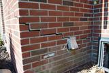 Large horizontal and stair-step cracks in the brick wall of a building’s exterior corner.