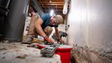 A worker kneels and uses a level to check the foundation in a basement under construction or repair.