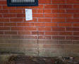 Cracked brick wall with a paper measuring guide taped above, highlighting foundation cracks in Denver.