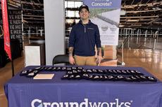 Man standing behind a Groundworks table with promotional materials and a "Sinking Concrete?" sign.