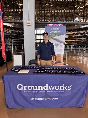 Man standing behind a Groundworks table with promotional materials and a "Sinking Concrete?" sign.