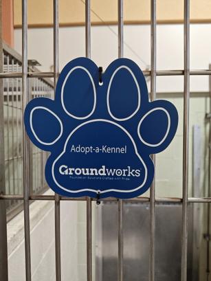 Blue paw-shaped sign on a kennel reads "Adopt-a-Kennel" and "Groundworks.