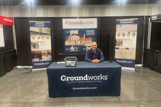 Man sitting at a Groundworks exhibition booth with banners and pamphlets on a table.