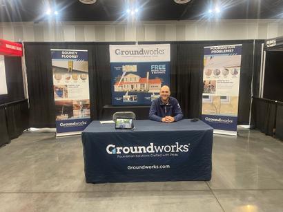 Man sitting at a Groundworks exhibition booth with banners and pamphlets on a table.