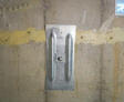 Steel wall anchor bolted to a concrete basement wall with yellow sealant along a horizontal crack.