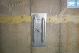Steel wall anchor bolted to a concrete basement wall with yellow sealant along a horizontal crack.