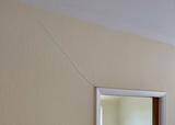 Diagonal wall crack above a door frame on a beige textured wall, likely caused by shifting from blue clay foundation.