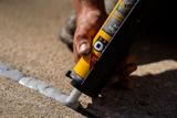 Hand applying gray caulk to a crack in concrete using a caulking gun for effective concrete crack repair on a sunny day.