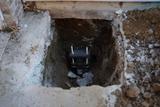 A deep rectangular hole in the ground with a metal foundation pier installed at the bottom to help prevent foundation cracking.