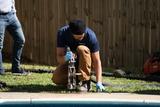 Person kneeling by a pool, using concrete lifting solutions with a power tool, wearing gloves and a beanie.