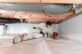 Worker in protective gear sealing a crawl space with plastic lining and insulation materials.