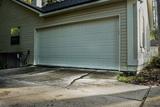 A concrete driveway with a large crack leading up to a closed garage door on a residential house.