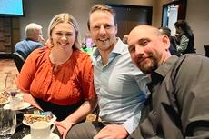 Three people smiling while seated at a table in a dimly lit room during an event.