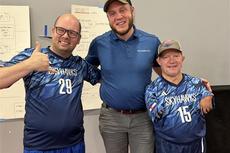 Three men smiling, two in Skyhawks sports jerseys, stand together on an indoor court.
