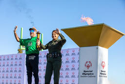 Two people holding a torch wave near a Special Olympics Southern California flame cauldron.