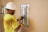 A construction worker in a hard hat adjusts a metal plate on a beige wall to address foundation damage.