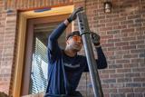 A person in safety glasses adjusts a metal foundation pier in front of a brick wall.