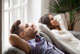 Two people relaxing on a couch by a window, enjoying fresh air.