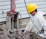 Worker in a yellow hard hat and white suit operates equipment at a construction site near a building.