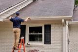 Person on a ladder measures gutter length—important for preventing foundation cracks.