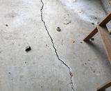 A large crack runs through a concrete foundation floor, with scattered debris and part of a wooden chair visible.