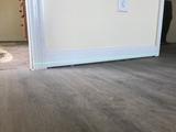 A green laser level line is projected across white baseboard trim in a room with wood flooring.